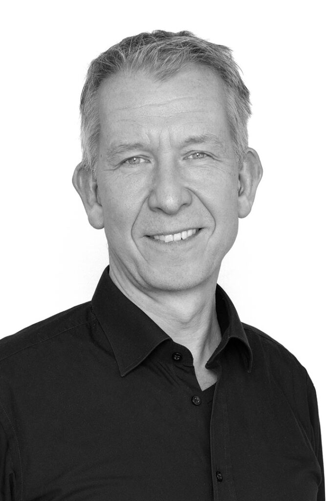 Portrætfoto i sort / hvid af indkøbschef og kontakt i Lithomex Søren Wilsbech i sort skjorte på hvid baggrund